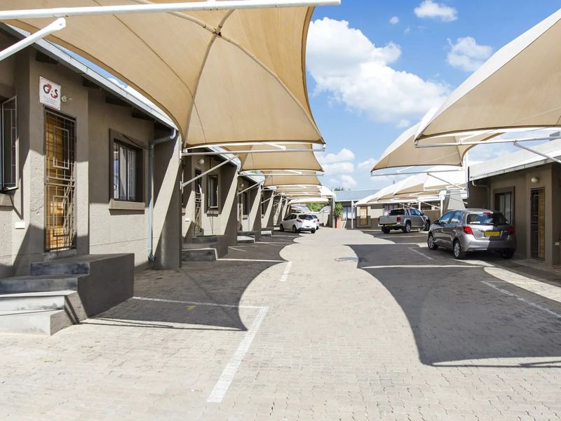 Exterior view of a townhouse complex featuring a paved driveway with multiple shade sail carports and secure unit entrances.
