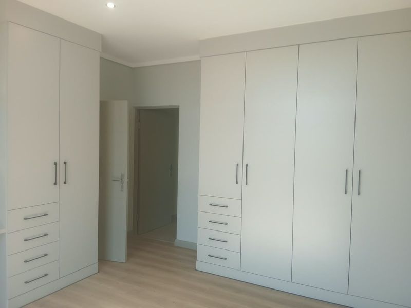 A bright, modern bedroom featuring extensive built-in cabinetry with ample storage and light-toned laminate flooring.