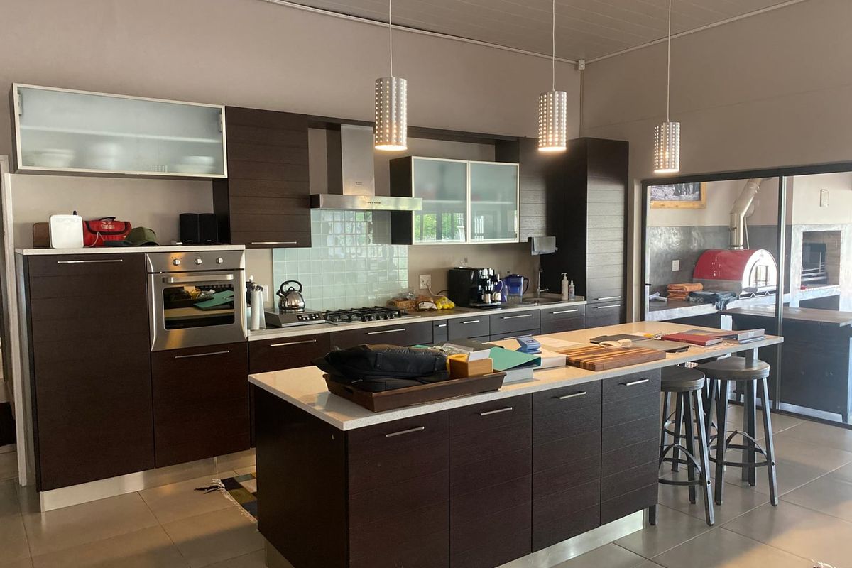 Modern open-plan kitchen featuring dark wood cabinetry, stone countertops, a central island, built-in oven, gas hob, and stainless steel extractor fan.