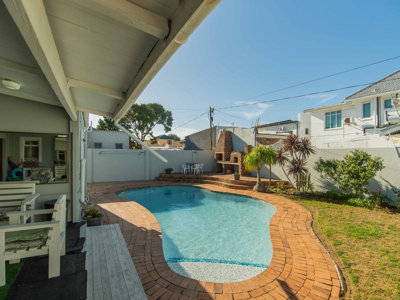 Outdoor pool area featuring a swimming pool with brick coping, a built-in brick braai, and a covered patio space.