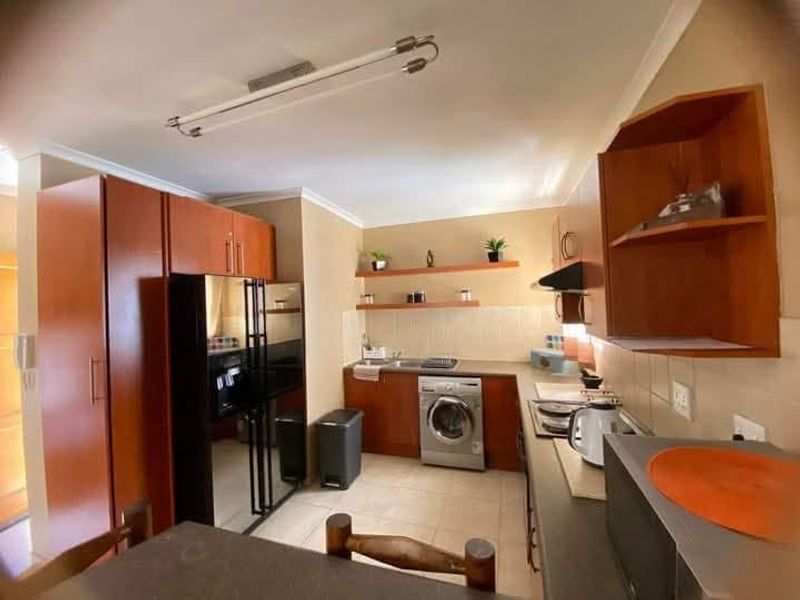A functional kitchen featuring wood-finish cabinetry, built-in appliances, tiled backsplash, and floating shelves, offering a practical layout for daily use.