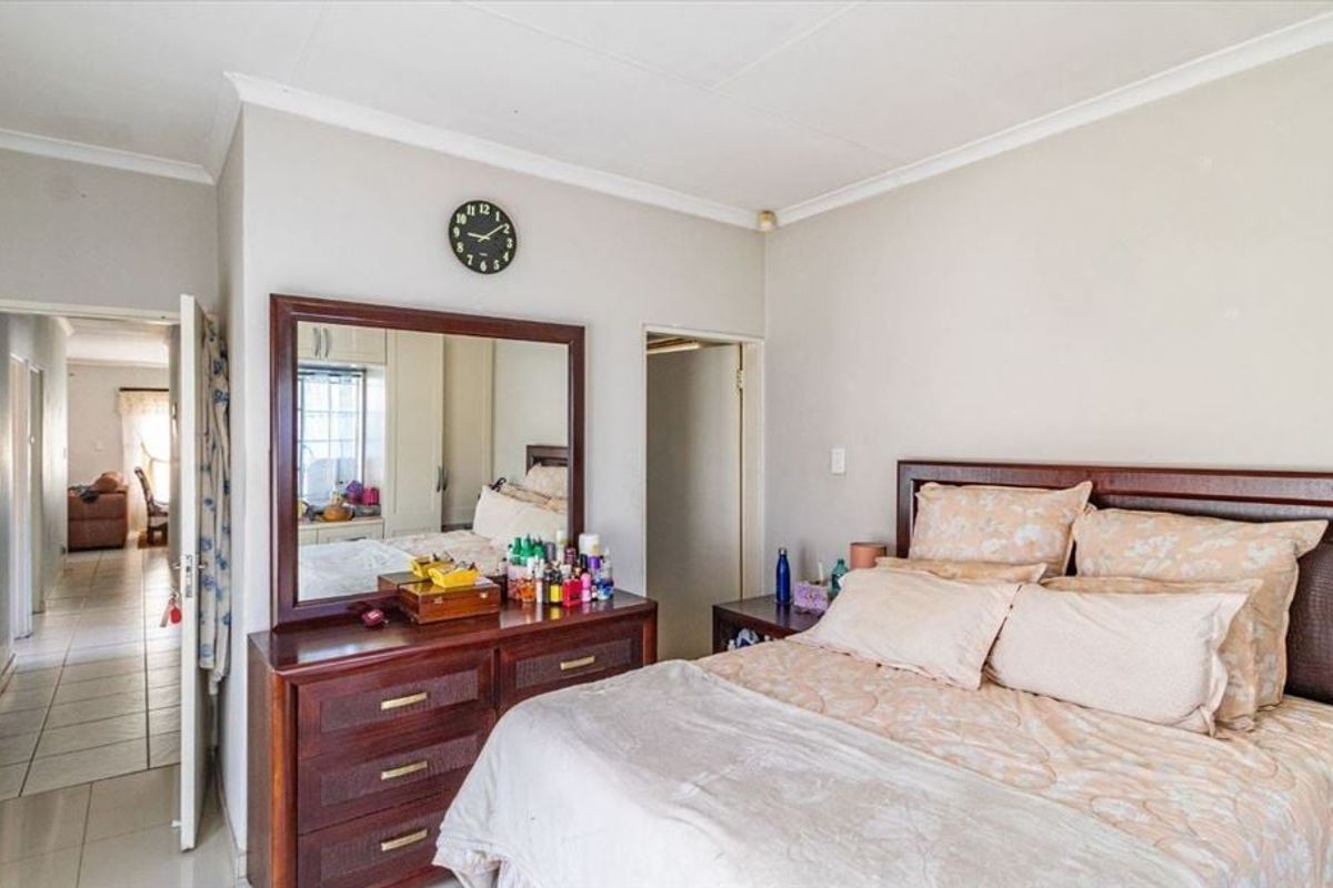 A spacious bedroom featuring tiled flooring, built-in cupboards, and cove cornice detailing, offering a functional layout with direct access to the hallway.