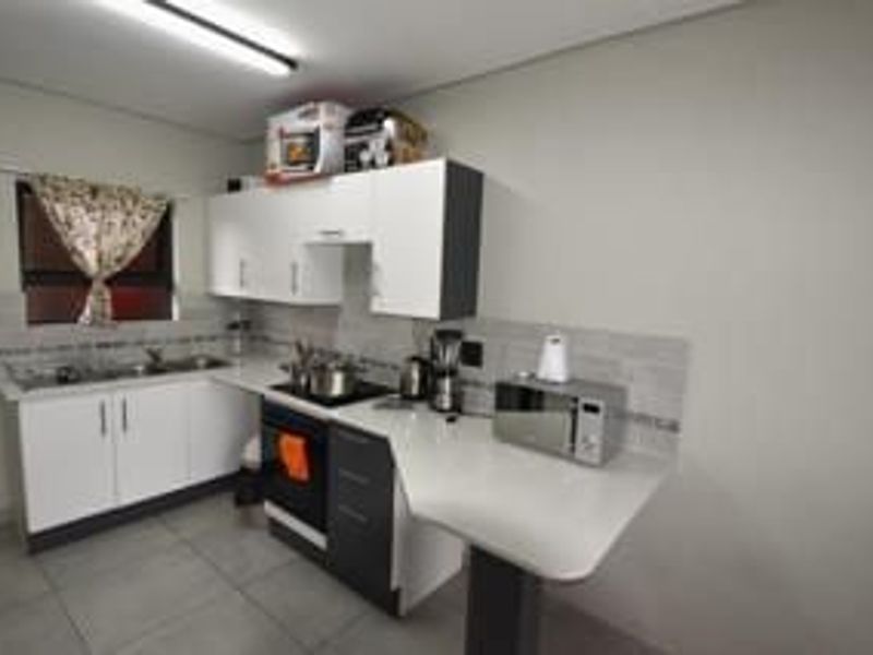 A functional kitchen featuring white and dark grey cabinetry, a tiled backsplash, built-in oven, hob, and a stainless steel sink.