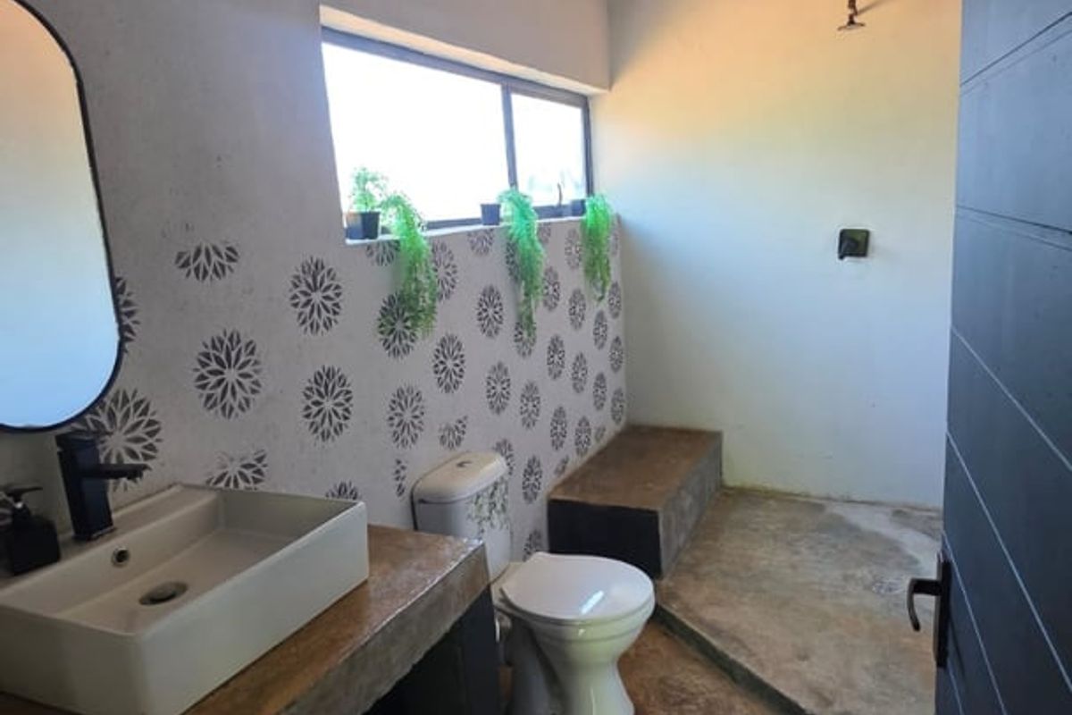 A rustic-style bathroom featuring a concrete vanity with a vessel sink, patterned wall tiles, and a walk-in shower area with concrete flooring.