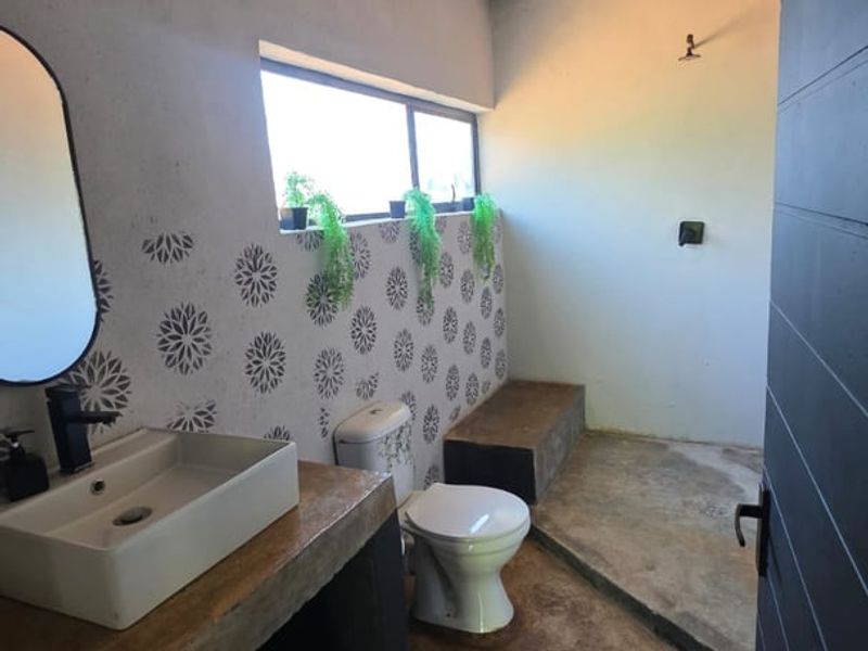 A rustic-style bathroom featuring a concrete vanity with a vessel sink, patterned wall tiles, and a walk-in shower area with concrete flooring.