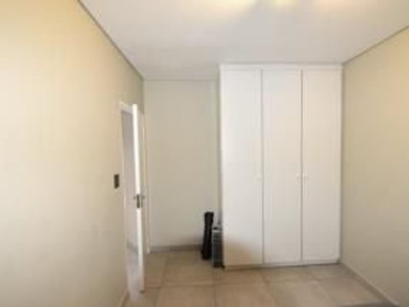 A clean, empty bedroom featuring neutral wall tones, tiled flooring, and white built-in cupboards providing ample storage space.