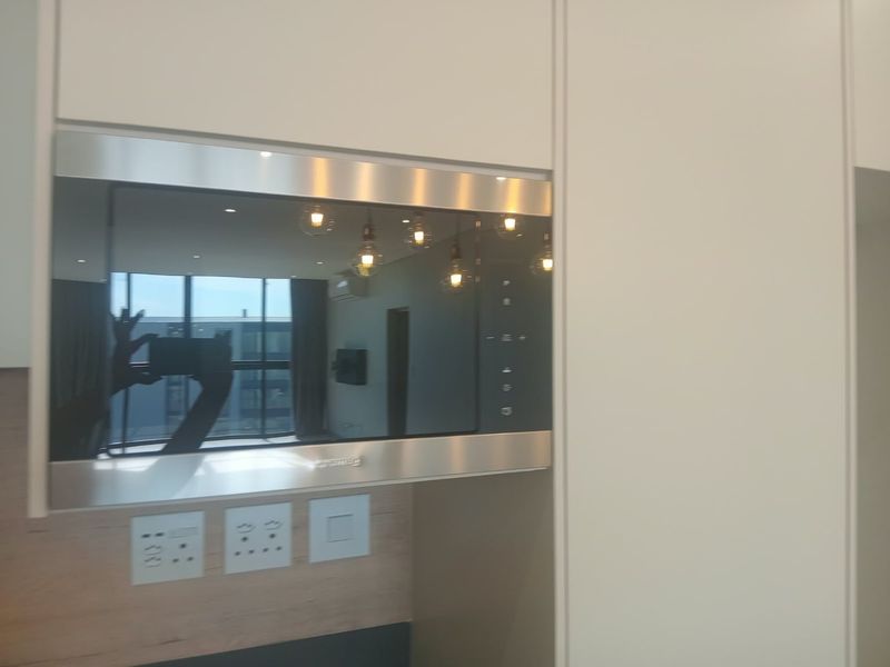 A close-up view of a modern built-in microwave integrated into sleek, light-colored kitchen cabinetry with visible electrical outlets below.