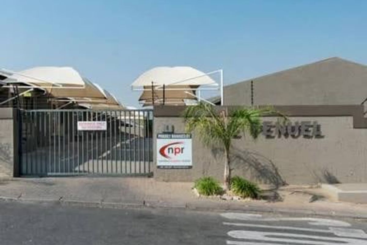 Front entrance view of the townhouse complex featuring a secure gated access point, paved driveway, and covered shade cloth parking bays.