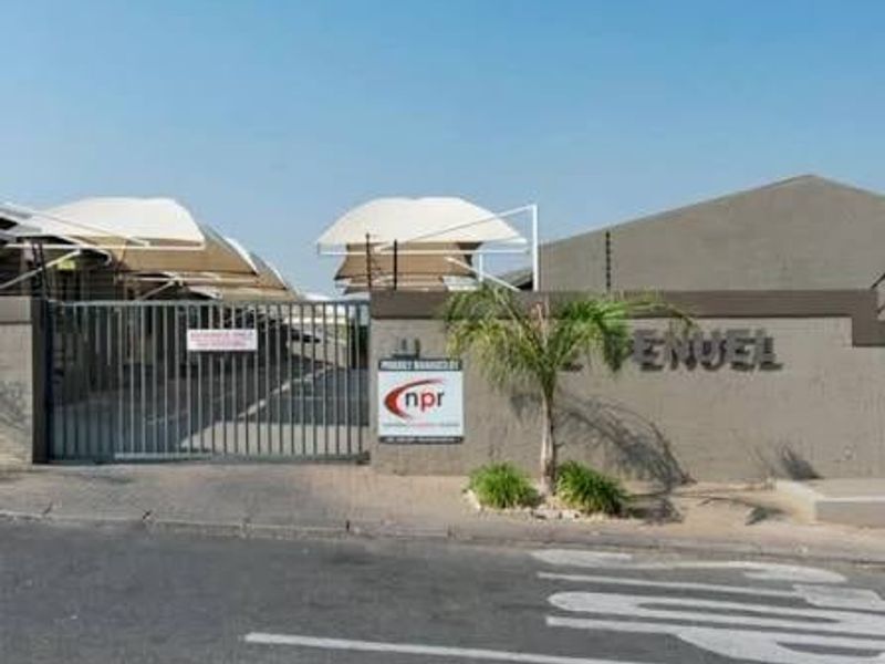 Front entrance view of the townhouse complex featuring a secure gated access point, paved driveway, and covered shade cloth parking bays.
