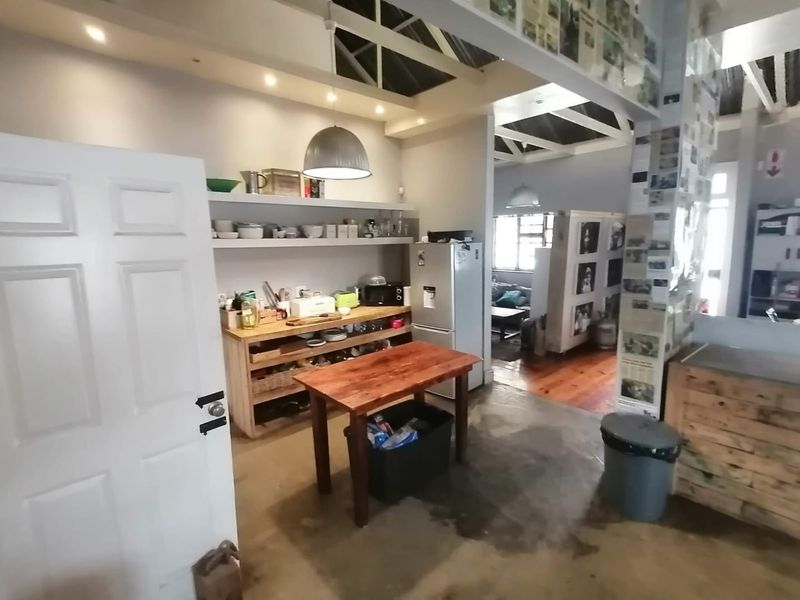 Open plan living area featuring exposed timber roof trusses, concrete flooring, and industrial-style lighting, offering a versatile space with potential for modern renovation.