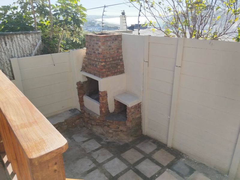 Outdoor patio area featuring a built-in brick braai, paved flooring, and enclosed by precast concrete boundary walls with electric fencing.