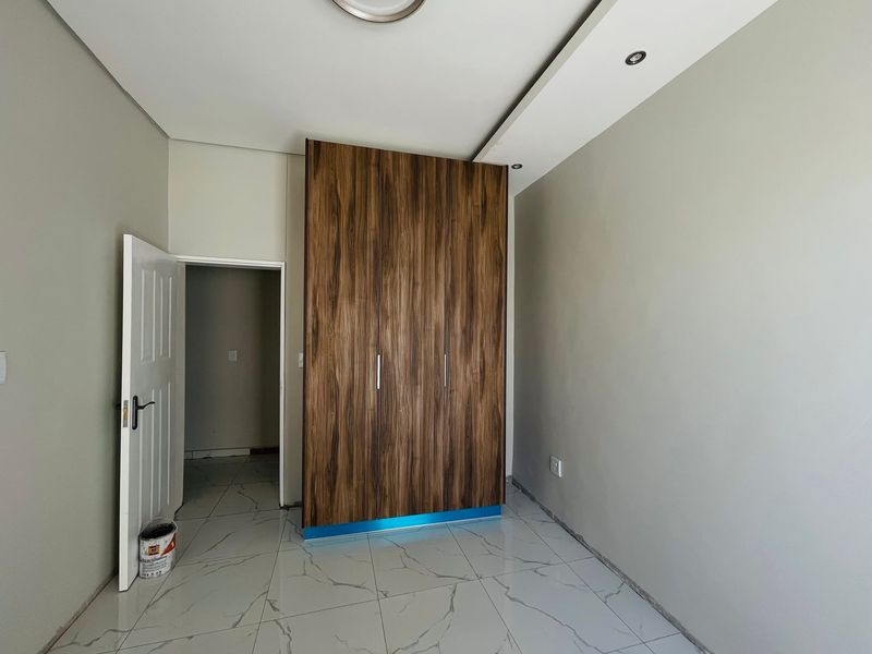 A clean, modern bedroom featuring large-format marble-look floor tiles, a contemporary wood-finish built-in wardrobe, and recessed ceiling lighting.