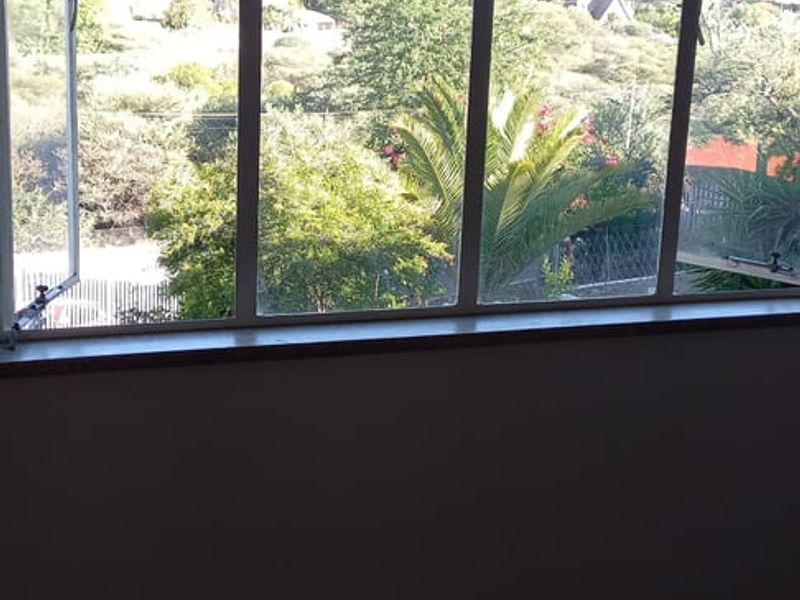 A view from an interior room featuring large metal-framed windows overlooking a landscaped garden and surrounding neighborhood.