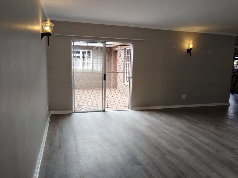 An empty living room featuring modern laminate flooring, neutral wall tones, and a sliding glass door with a security gate leading to an outdoor area.