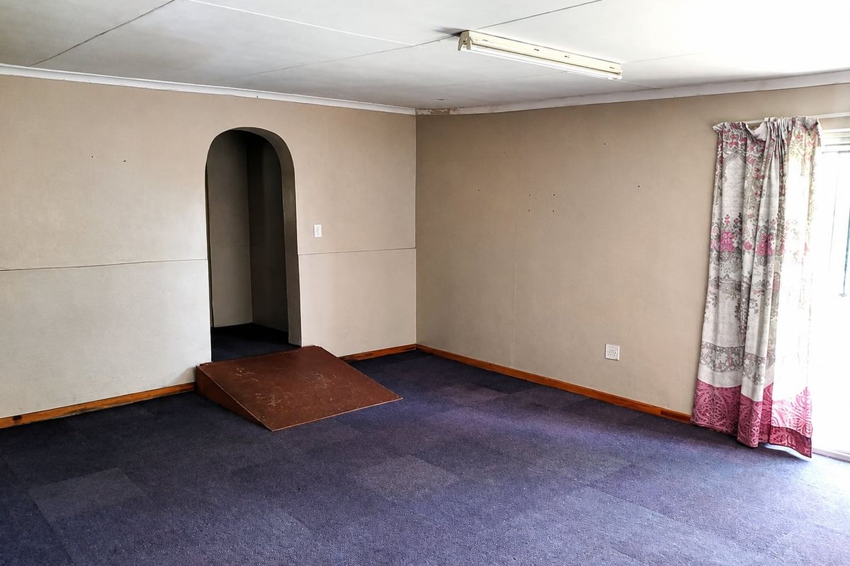 An empty living room featuring a unique arched doorway with a ramp, carpeted flooring, and access to an outdoor area.