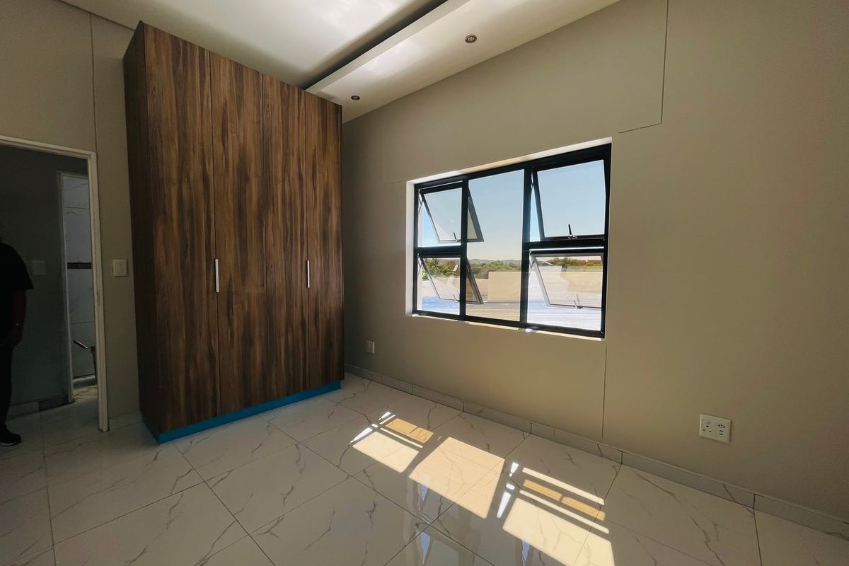 A bright, modern bedroom featuring large-format marble-look floor tiles, a sleek built-in wooden wardrobe, and recessed ceiling lighting.