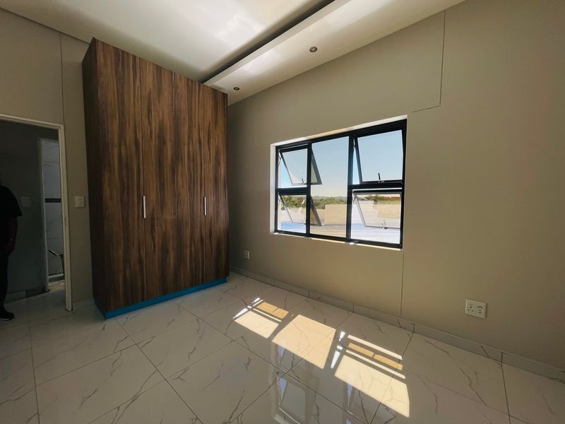 A bright, modern bedroom featuring large-format marble-look floor tiles, a sleek built-in wooden wardrobe, and recessed ceiling lighting.
