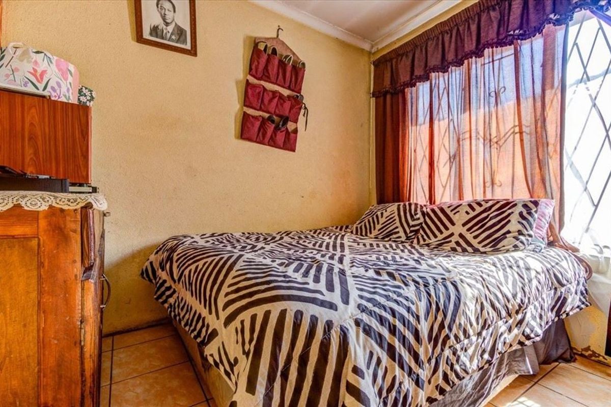 A compact bedroom featuring tiled flooring and a window fitted with security bars, offering a functional space with potential for cosmetic updates.