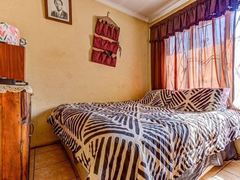 A compact bedroom featuring tiled flooring and a window fitted with security bars, offering a functional space with potential for cosmetic updates.