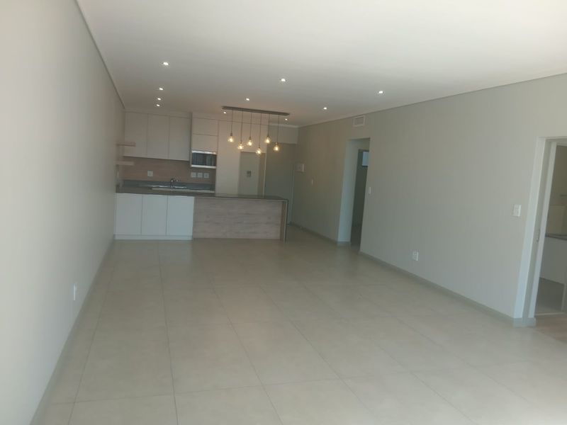 A spacious open-plan living and kitchen area featuring modern cabinetry, a central island, recessed lighting, and neutral tiled flooring throughout.
