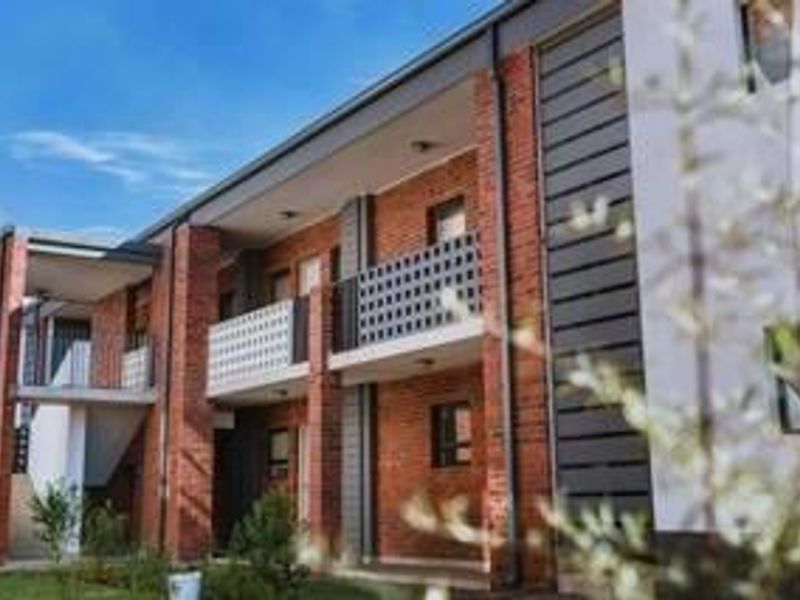 A view of the apartment building exterior featuring brick facade detailing, private balconies with railings, and an external stairwell.