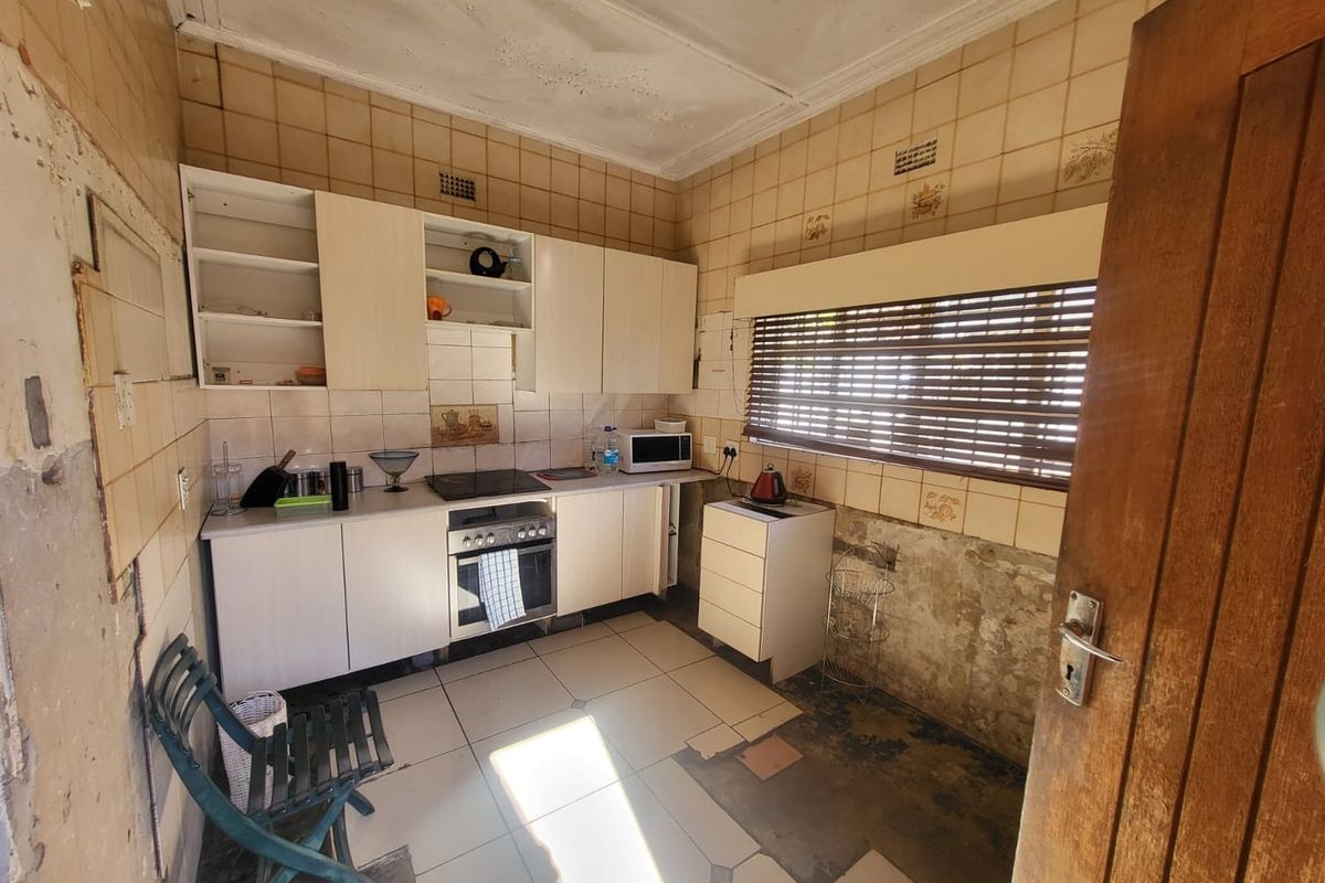 A dated kitchen requiring significant renovation, featuring built-in cabinetry, an electric hob, and oven, with visible damage to wall finishes and flooring.