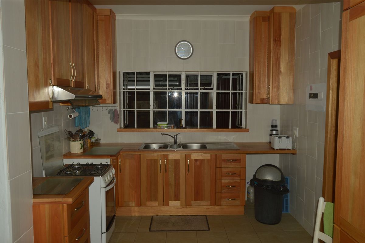 A functional kitchen featuring wooden cabinetry, a double bowl sink, gas stove with extractor fan, and tiled finishes throughout.