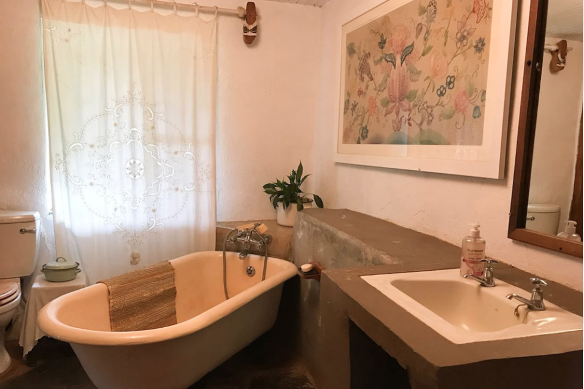 A rustic bathroom featuring a vintage freestanding bathtub, a custom built-in vanity with a ceramic sink, and a toilet.