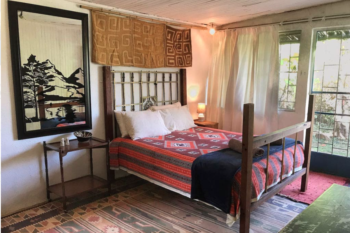 A rustic bedroom featuring a timber-paneled ceiling, direct access to the exterior via a security gate, and large windows allowing natural light.