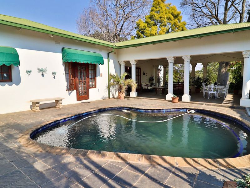 Outdoor pool area featuring a swimming pool, covered patio with classical columns, and tiled flooring, perfect for relaxation and entertaining.