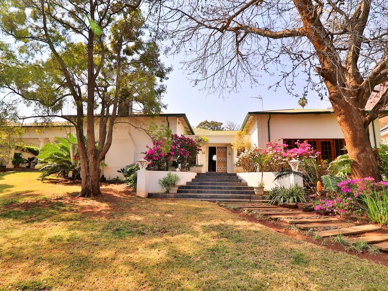 Charming front elevation of a single-story residence featuring a landscaped garden, stone steps leading to the entrance, and mature trees.