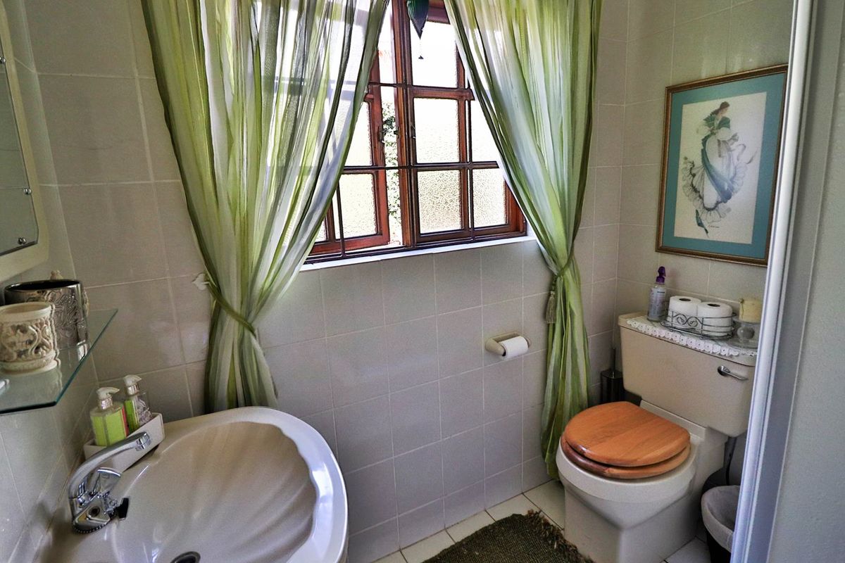 A compact bathroom featuring ceramic wall and floor tiling, a pedestal basin, and a timber-framed window.