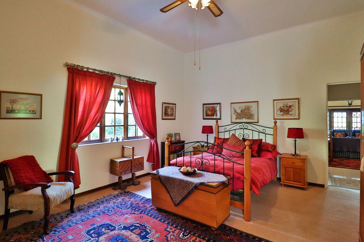 A spacious bedroom featuring a ceiling fan, timber-framed windows, and neutral carpeting, offering a comfortable and well-maintained living space.