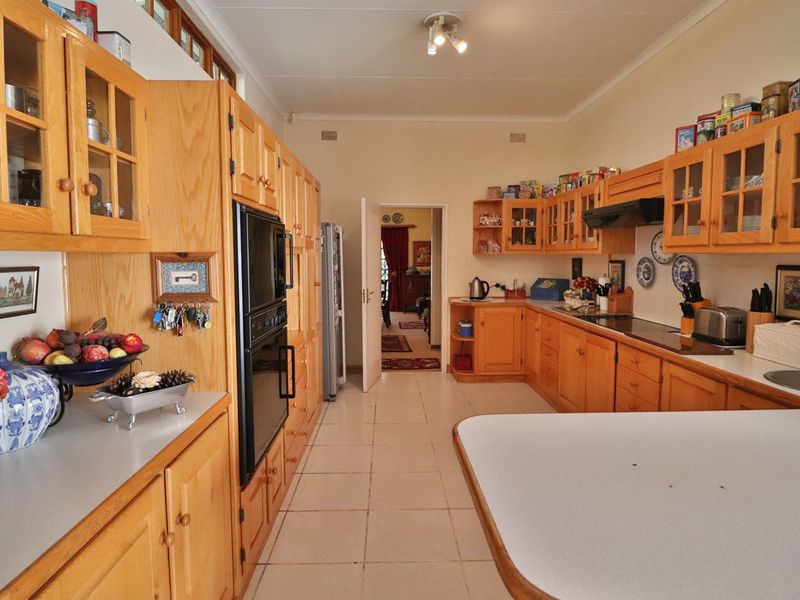 A spacious kitchen featuring extensive wooden cabinetry, built-in oven, extractor fan, and tiled flooring, offering a functional layout with ample storage space.