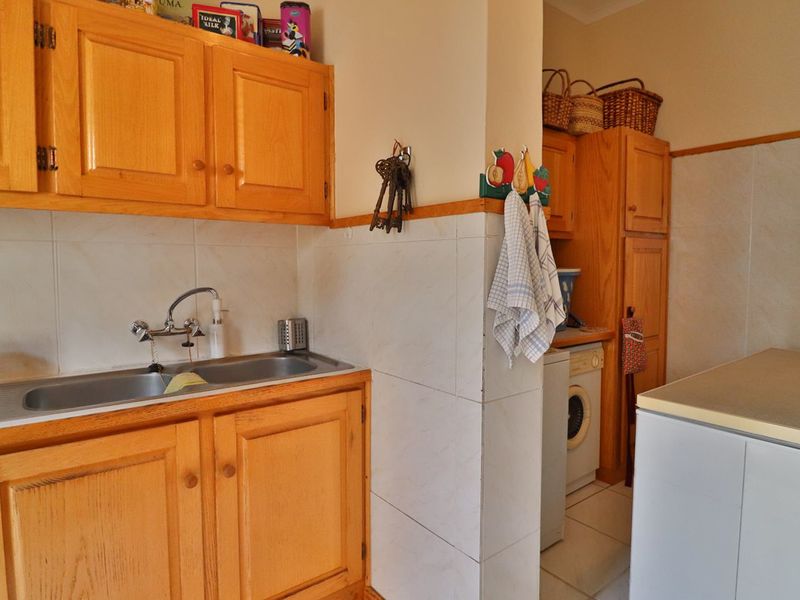 A functional laundry area featuring built-in wooden cabinetry, a double stainless steel sink, and tiled splashbacks with space for laundry appliances.