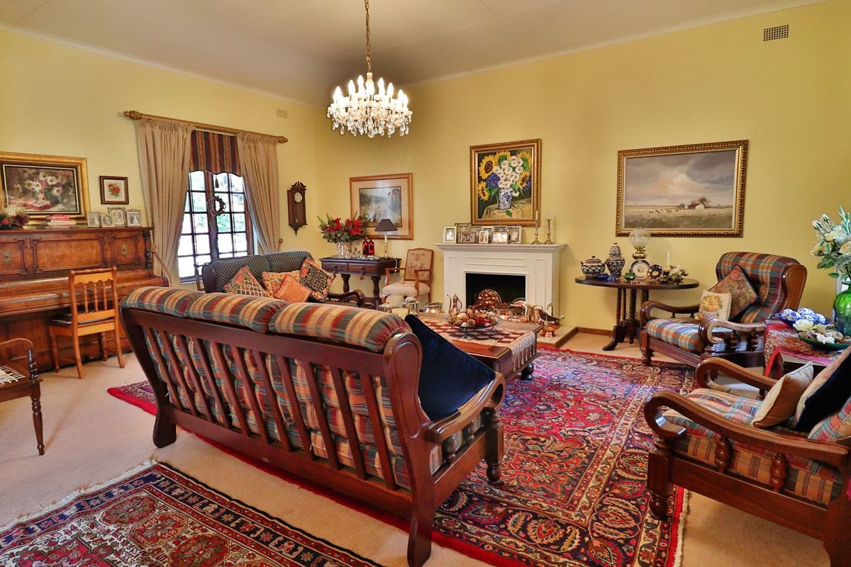 A traditional living room featuring a fireplace with a mantelpiece, a crystal chandelier, and an arched window.