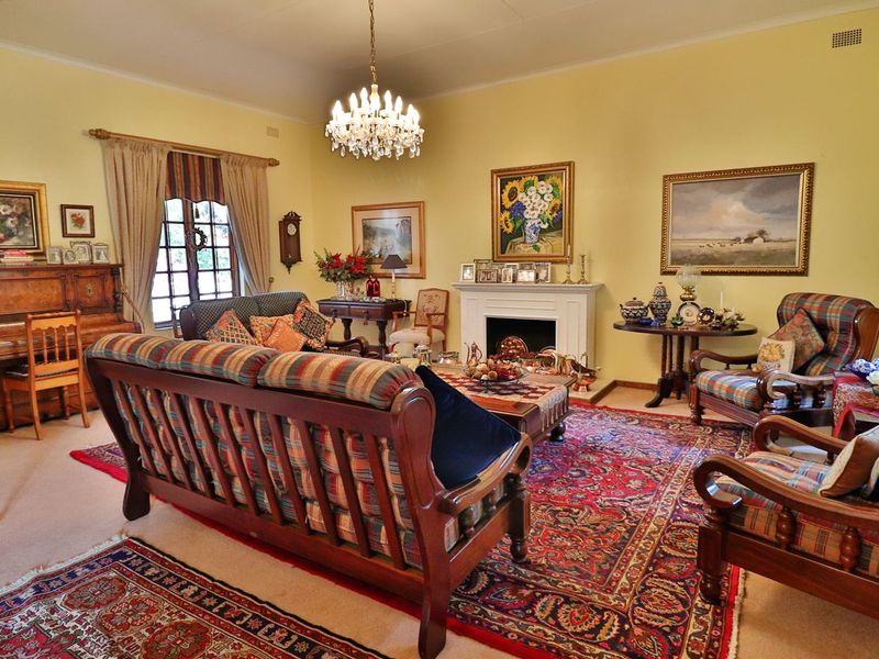 A traditional living room featuring a fireplace with a mantelpiece, a crystal chandelier, and an arched window.