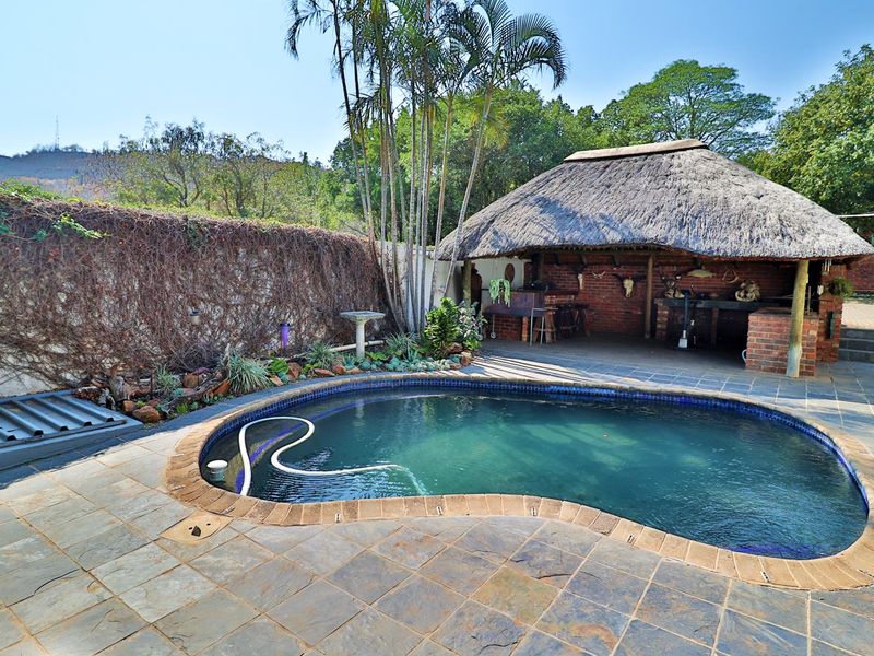 Outdoor entertainment area featuring a swimming pool, slate paving, and a traditional thatched lapa with a built-in brick braai.