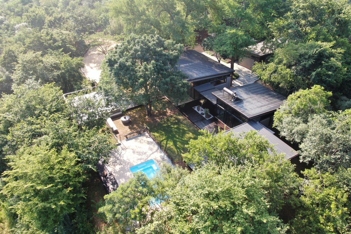 Aerial view of a modern property nestled in a lush, wooded setting, featuring a swimming pool, timber decking, and multiple interconnected building structures.