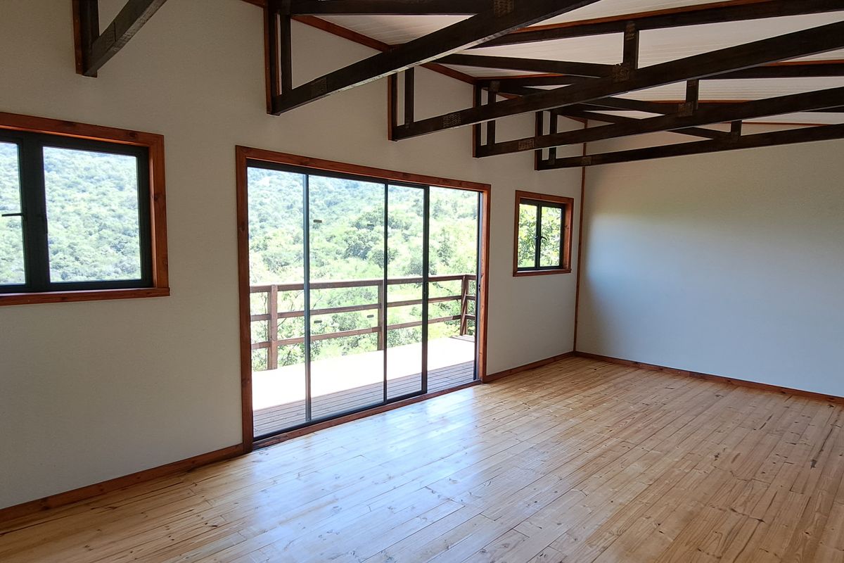 Spacious living area featuring exposed timber roof trusses, polished wooden flooring, and large sliding glass doors opening onto a scenic outdoor deck.