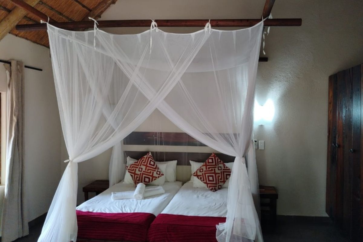 A cozy bedroom featuring a traditional thatched roof with exposed timber rafters, tiled flooring, and a built-in wardrobe.