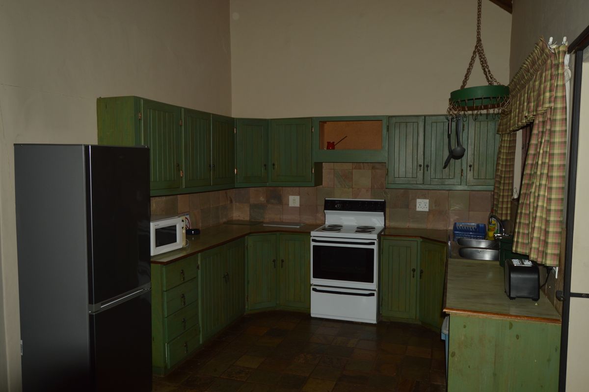 A dated kitchen featuring green timber cabinetry, stone tile backsplash, stone flooring, and a freestanding stove under a high vaulted ceiling.