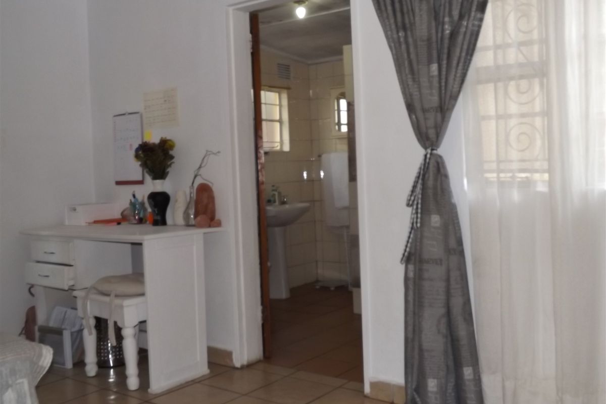 A bedroom featuring tiled flooring and security bars on the window, with an adjoining bathroom visible through the doorway.