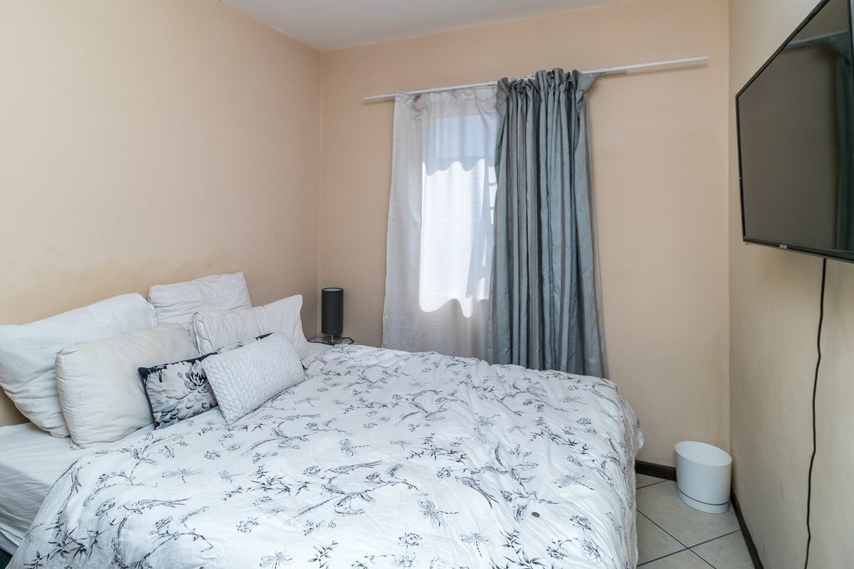 A compact bedroom featuring tiled flooring, a wall-mounted television, and a window with curtain rod installation.