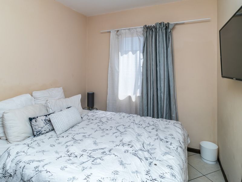 A compact bedroom featuring tiled flooring, a wall-mounted television, and a window with curtain rod installation.