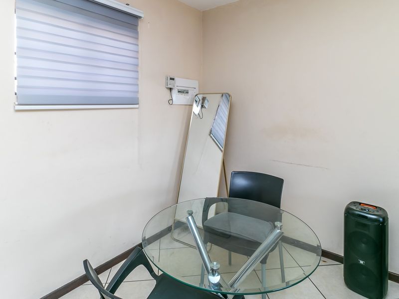 A functional living area featuring tiled flooring, a window with a roller blind, and a wall-mounted electrical distribution board.