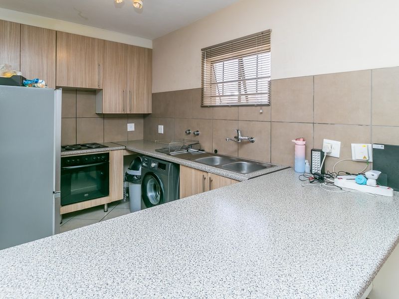Functional kitchen featuring wood-look cabinetry, granite-style countertops, integrated oven and hob, and a double sink with tiled splashbacks.