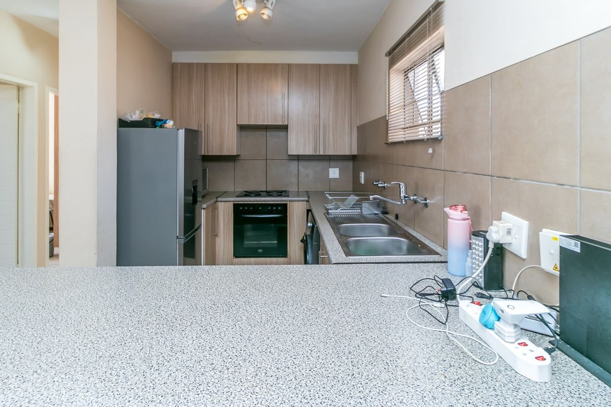 A functional kitchen featuring wood-look cabinetry, a built-in oven and hob, double stainless steel sink, and a granite-look breakfast bar counter.