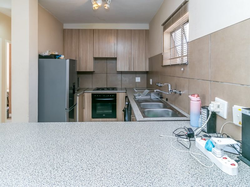 A functional kitchen featuring wood-look cabinetry, a built-in oven and hob, double stainless steel sink, and a granite-look breakfast bar counter.