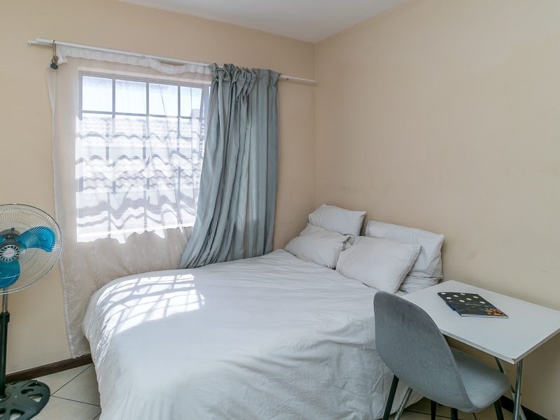A compact bedroom featuring tiled flooring and a window with curtain rod, providing a functional space for rest.